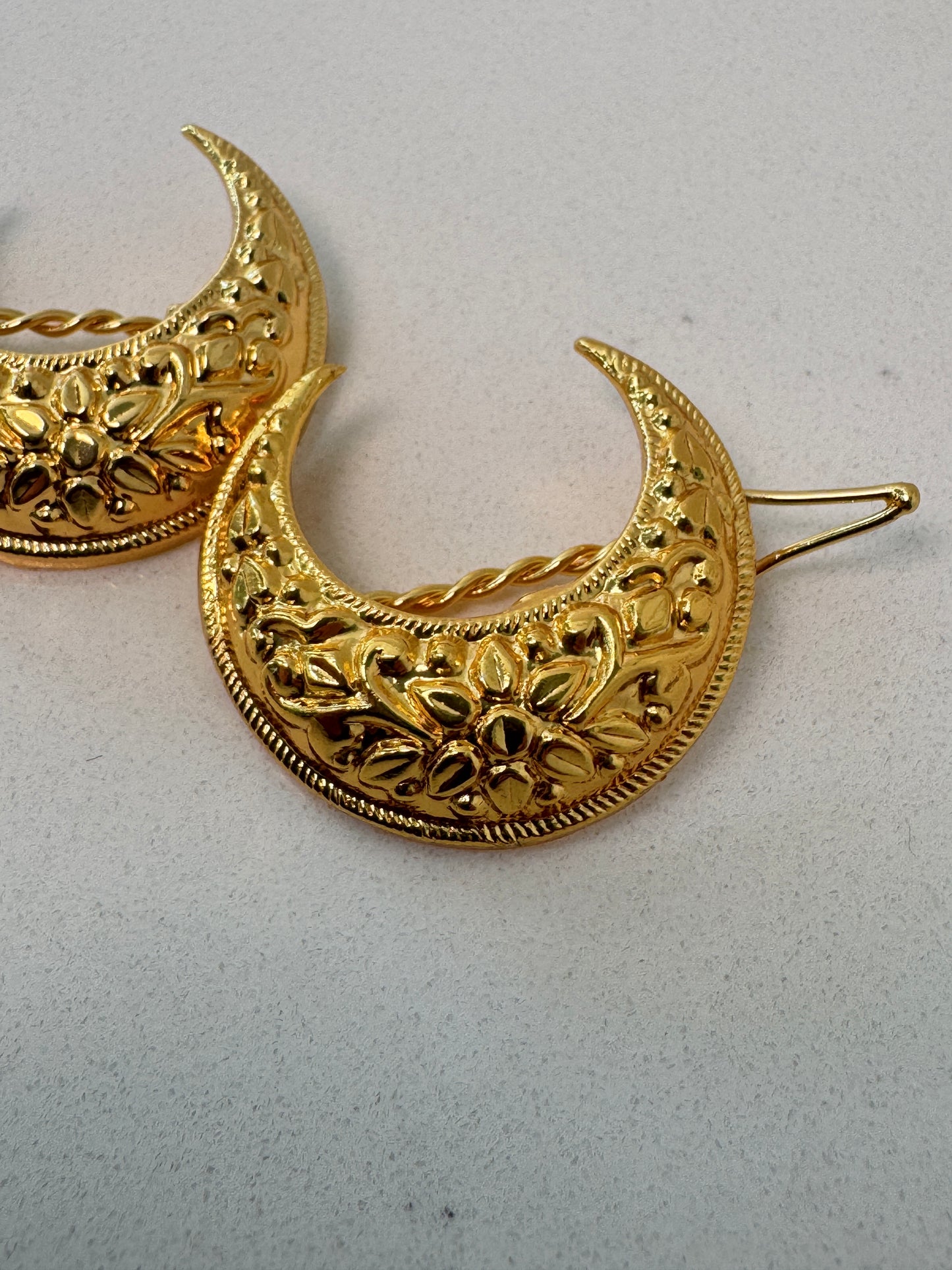 Gold crescent-shaped hair pins on a light gray background