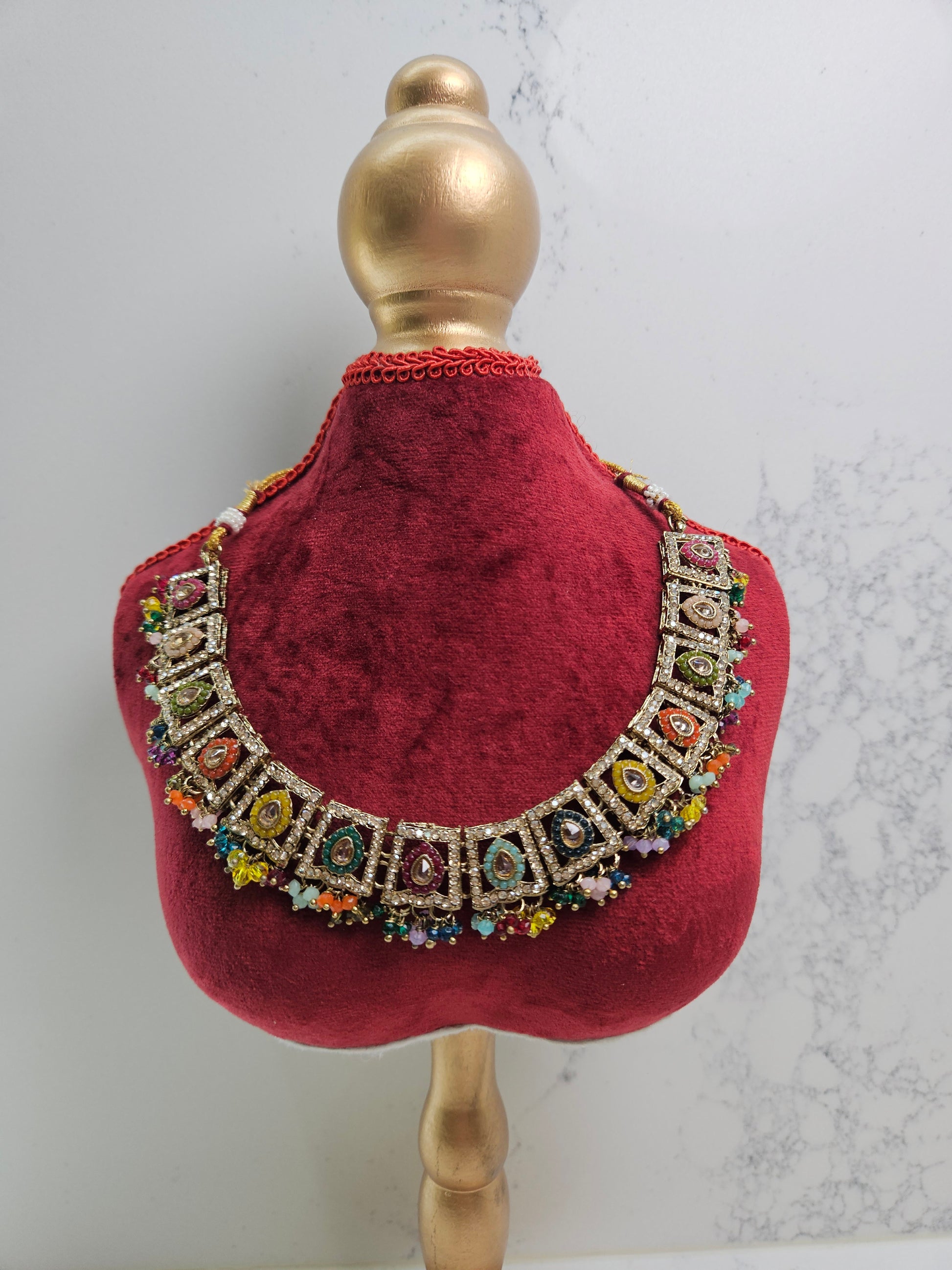 Decorative red velvet collar with colorful gemstones on a mannequin head against a light background