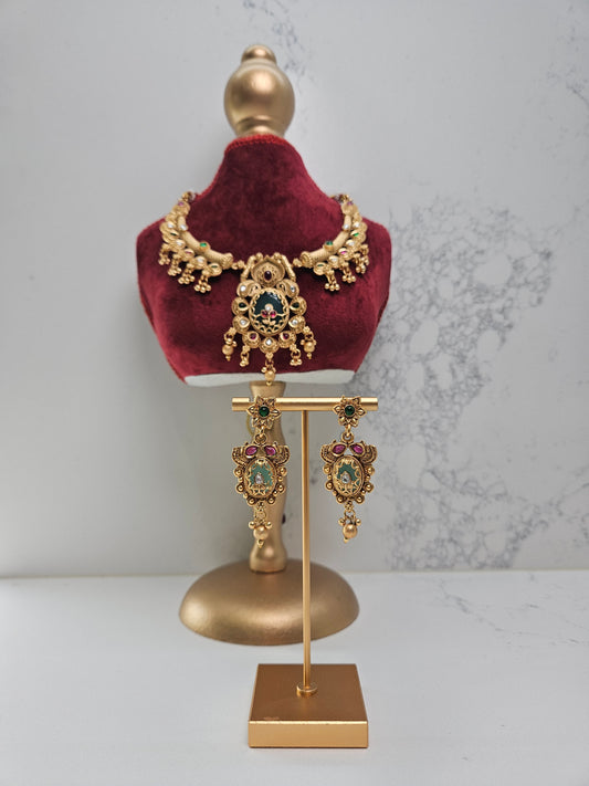 Gold necklace and earrings on a mannequin bust with a gold stand against a marble background