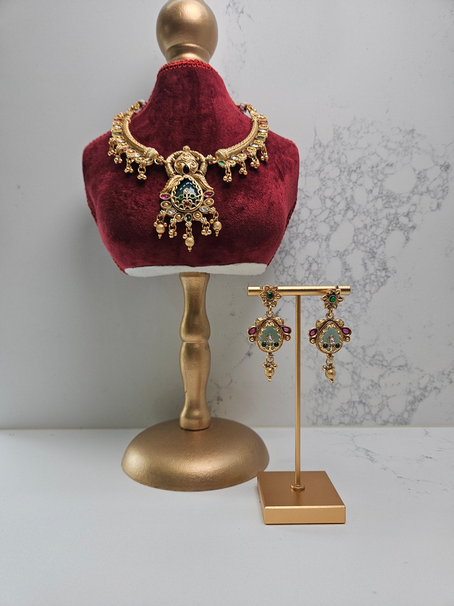 Gold necklace and earrings on a mannequin bust and gold stand against a marble background