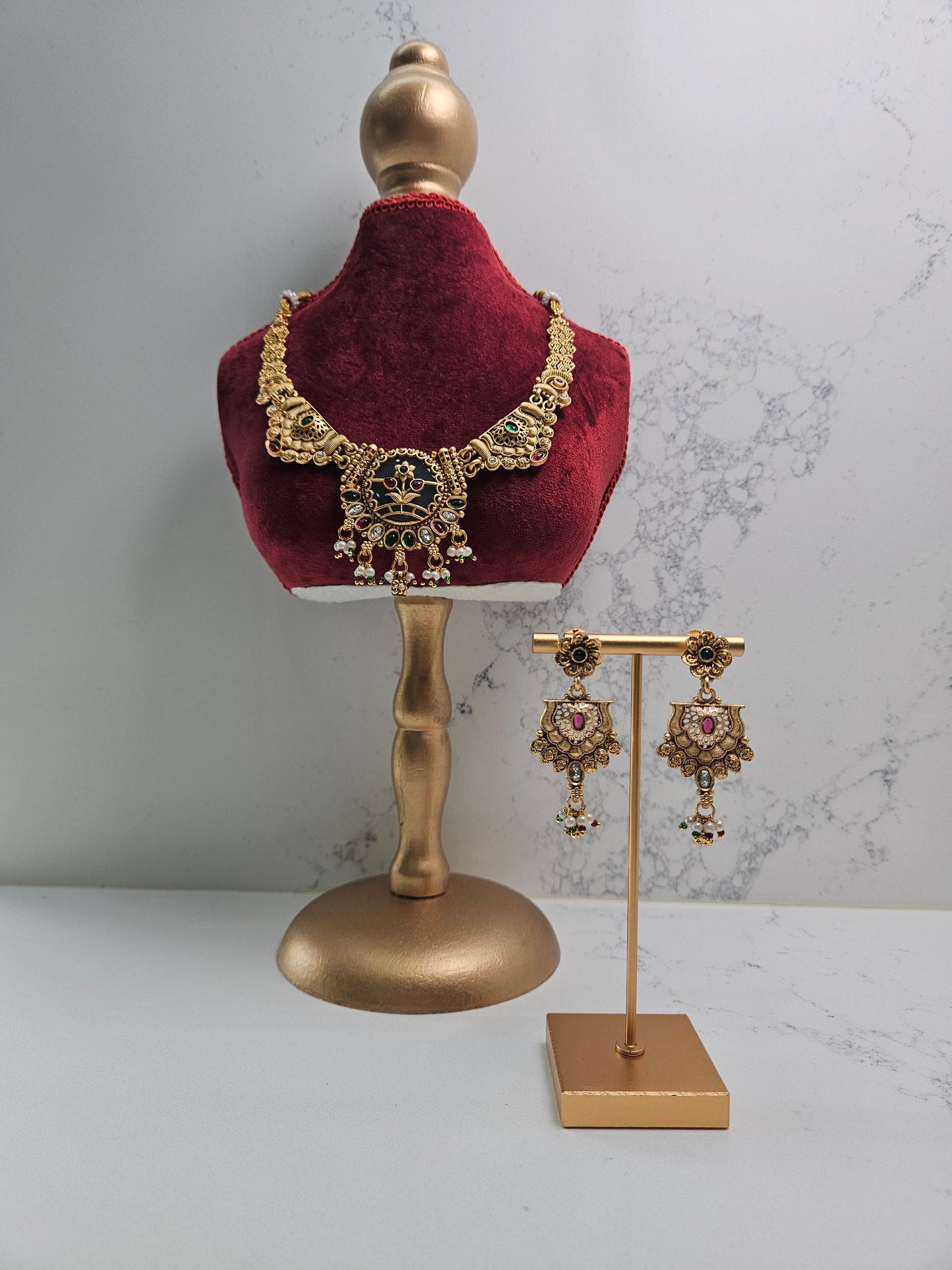 Gold necklace and earrings on a red velvet mannequin bust with a marble background